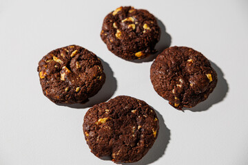 A flat lay of four dark chocolate cookies with visible nut chunks, arranged neatly on a white surface. No branding or packaging is visible