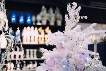 Close-up of a white artificial Christmas tree with pastel ornaments and string lights in a festive retail display. Holiday retail styling, pastel Christmas decor, winter gift aesthetics