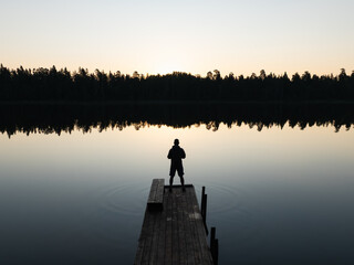 Aerial drone view of a person's silhouette on a wooden pier overlooking a tranquil Estonian lake...