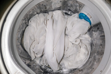 White clothes being washed in a washing machine with soap bubbles. Perfect for detergent ads, household cleaning articles, or laundry service promotions
