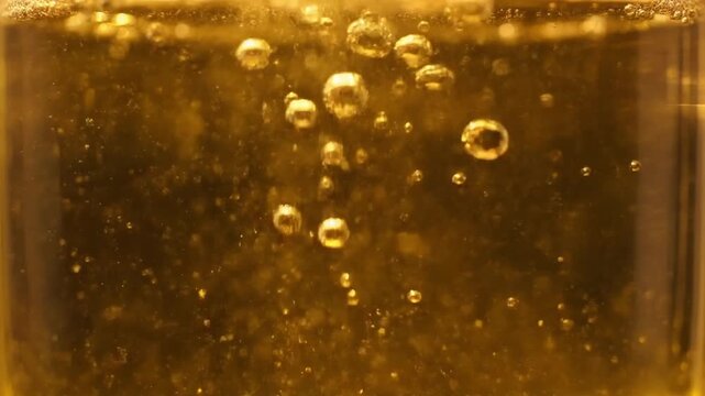 Close-up of carbonated amber liquid with rising bubbles in a cylindrical glass container on a white background.