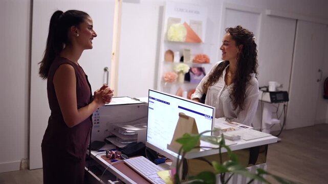 Welcoming receptionist attentively listening to a patient at the front desk of a modern beauty or medical clinic, providing excellent customer service and information before an appointment