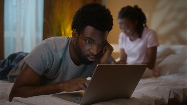 African American family couple working laptop digital tablet evening at home bedroom ethnic married wife husband using computer typing device online gadget addiction shopping reading news indoor night