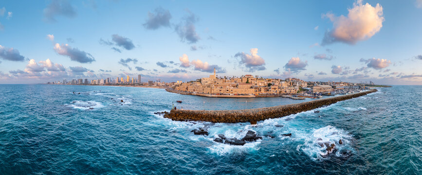 Aerial view of the ancient port city with its stone breakwater embracing the turquoise sea against the backdrop of modern skyscrapers, Old Jaffa, Tel Aviv-Yafo, Israel.