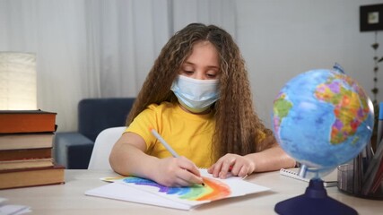 Girl drawing colorful rainbow on paper wearing mask at desk with globe and book showing child engaged in home school education activity creating bright drawing and learning about world and geography - Powered by Adobe