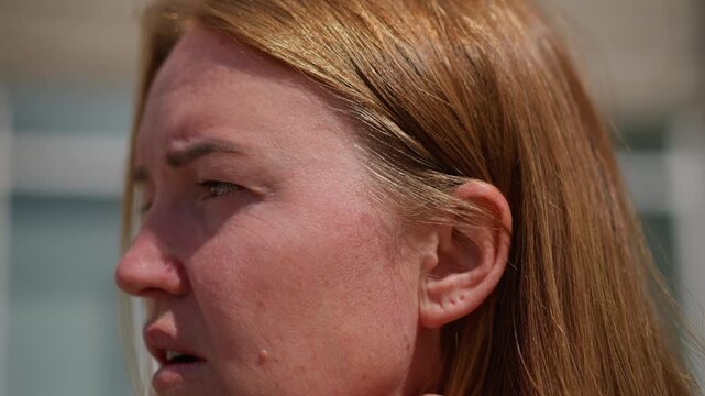 Close up of worried woman adjusting hair under bright sunlight, revealing emotional tension and introspection, natural light highlights texture of hair and subtle facial lines