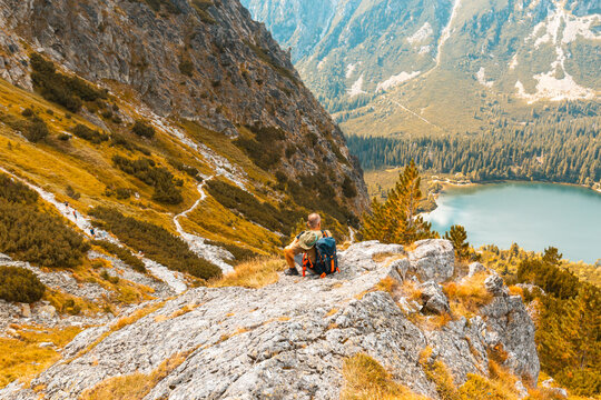 Alone tourist resting on a mountainside and enjoys a beautiful autumn mountain landscape with a lake - Powered by Adobe