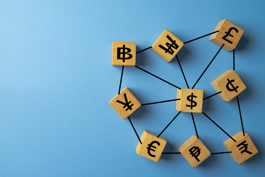 Top view flat lay of currency symbols on wooden blocks, connected in a web. Concept of international payments, global economy, and financial technology (Fintech). Blue background with copyspace.