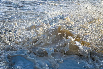 Close-up of foaming sea spray and water droplets in golden light, capturing wild, turbulent Irish Sea energy.