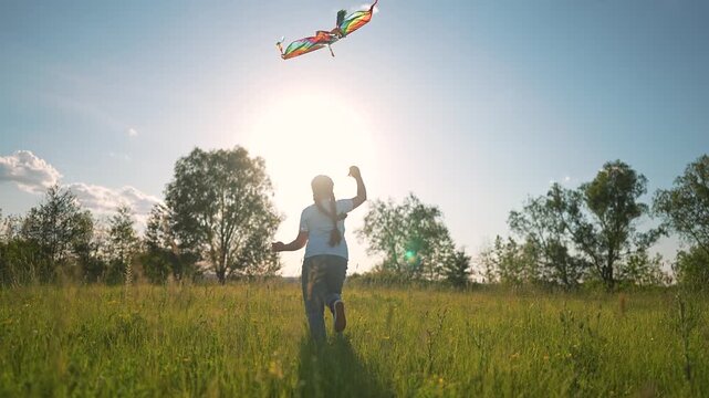 Girl running outdoors with rainbow kite. Summer field bright with grass. Kite dances giving girl freedom. Happy girl plays under sun. Rainbow kite twirls over grass. Girl enjoys playful field outdoors