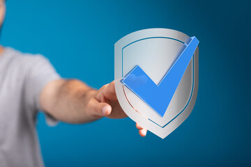 A person's hand holding a shield with a check mark, symbolizing validation, approval, and security....