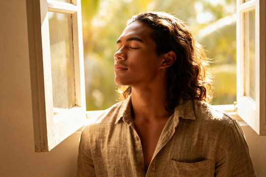 A young man enjoys a peaceful moment by the open window, soaking up natural light while taking a break from digital distractions. Digital detox and slow life concept - Powered by Adobe