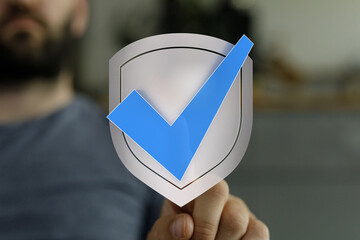 A man's hand holding a shield with a blue checkmark symbolizing protection, security, and approval....