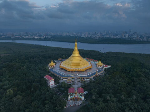 Aerial view of the radiant golden Global Vipassana Pagoda nestled amidst verdant foliage, contrasting against the distant cityscape, Borivali, Mumbai, Maharashtra, India.