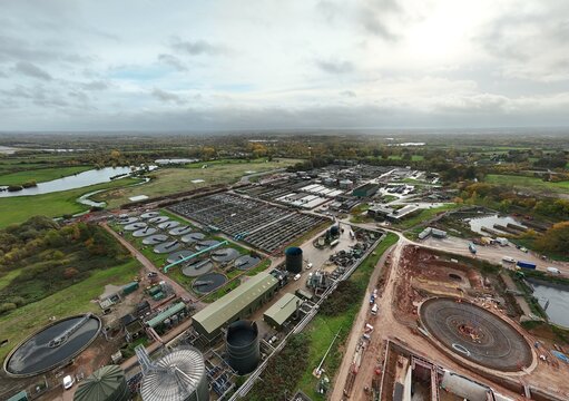 Aerial view of the sprawling industrial complex, where circular tanks and rectangular grids meet the horizon under a vast, clouded sky, Leicester, England, United Kingdom.