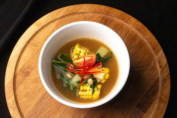 Sayur Asem Indonesian Vegetable Soup with Corn, Tomato, Long Bean, Chayote with Tamarind Broth and Spices on Top of Circle Wooden Table and Black Background