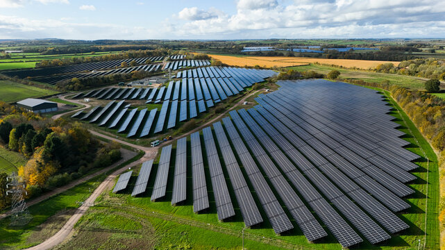 Aerial view of solar panels gleaming under the sunlight, contrasting with the green fields and distant trees, Mansfield, England, United Kingdom.