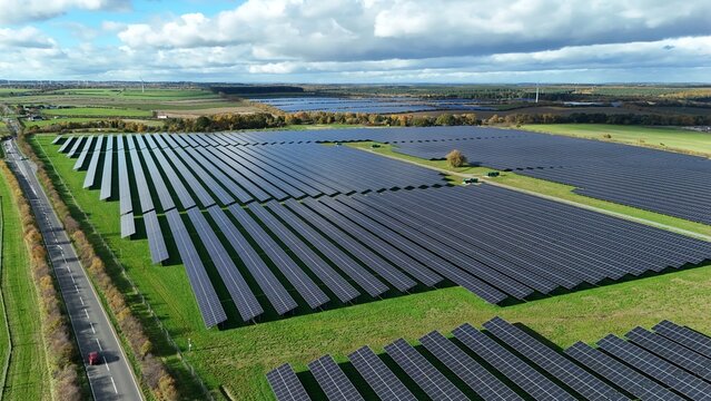 Aerial view of rows of dark solar panels contrast with the lush green fields under a sky of white clouds, creating a stark juxtaposition of energy and nature, Mansfield, England, United Kingdom. - Powered by Adobe