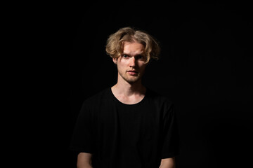 Fototapeta premium Concerned man in black shirt staring ahead with tense expression in low key lighting