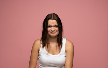 Obraz premium Studio portrait of young woman frowning with confused facial expression on pink background