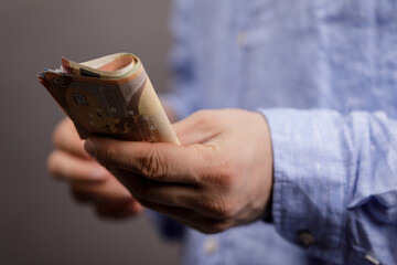 Close-up shot of a man's hand holding a stack of folded euro banknotes, symbolizing wealth,...