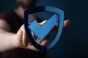 A person's hand holding a glowing blue shield with a check mark, representing protection, security,...