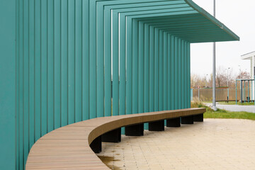 Curved wooden bench under teal metal canopy creates striking urban space, highlighting modern...
