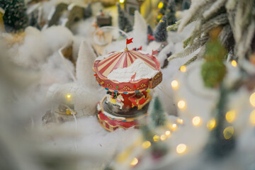 miniature Christmas carousel covered in fake snow with soft bokeh lights in a winter village display concept of holiday decoration, festive retail, seasonal entertainment