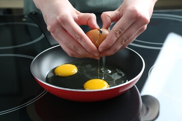 Woman cracking egg into frying pan in kitchen, closeup