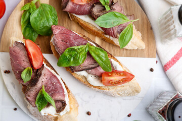 Delicious bruschettas with roast beef served on white table, flat lay