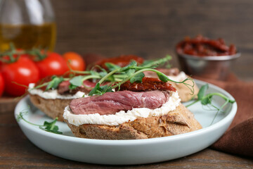 Delicious bruschettas with roast beef served on wooden table, closeup