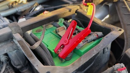 red jumper cable clamp connected to car battery terminal. Ideal for automotive repair, battery charging, power, and emergency or safety tutorial videos.
