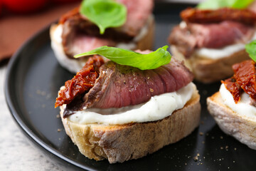 Bruschettas with roast beef, cream cheese, basil and sun-dried tomato on table, closeup