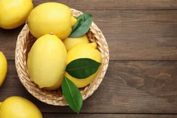 Fresh lemons with green leaves and wicker basket on wooden table, flat lay. Space for text