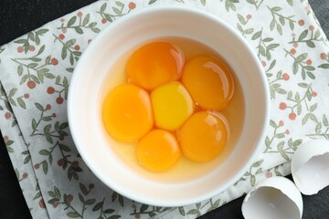 Fresh egg yolks in bowl on black table, top view