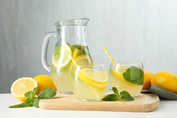 Fototapeta premium Fresh lemonade in glasses, jug, lemons and mint on white table