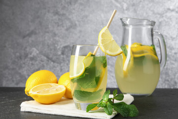 Fresh lemonade in glass, jug, lemons and mint on black table, closeup