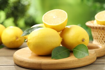 Fresh lemons with green leaves on wooden table outdoors, closeup