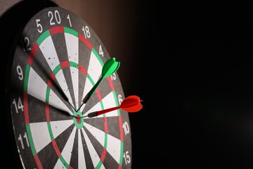 Dartboard with darts on black background, closeup. Space for text