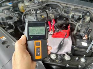 Close-up of Technician Testing AGM Car Battery Voltage and Condition with Digital Tester Tool in Garage.