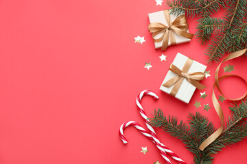 Fir tree branches, gifts and Christmas decor on red background, flat lay. Space for text
