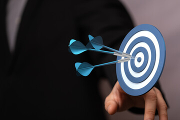 Close up of a businessman's hand reaching towards a dart board with darts in the bullseye. Concept...