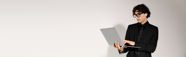 Stylish young man works on laptop in fashionable attire against a minimalist backdrop