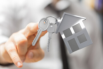 A person's hand holding keys with a house-shaped keychain, representing new home, buying a house,...