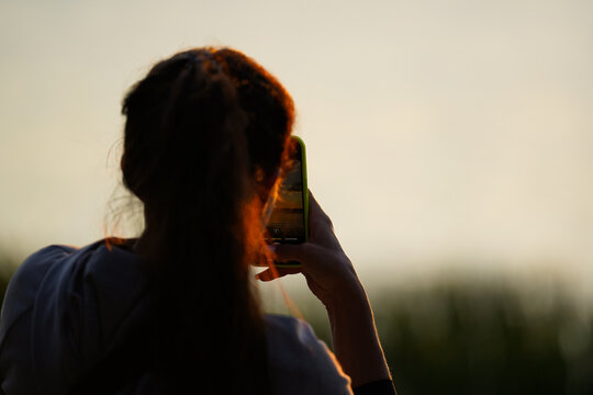Woman taking photo with smartphone at sunset - Powered by Adobe