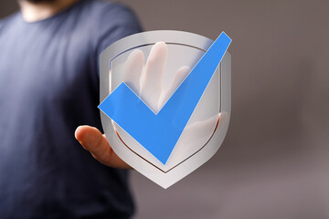 A person's hand holding a digital shield with a blue check mark, representing concepts like...