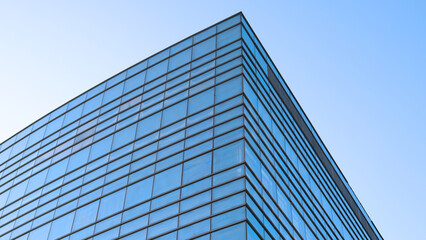 Glass facade of contemporary building reflecting clear blue sky