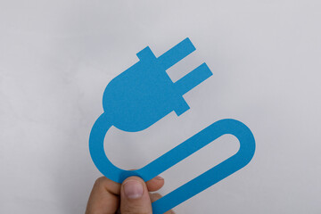 Hand holding blue cutout of a power plug against a white background. Symbol of electricity, sustainable energy and connection. Ideal for renewab
