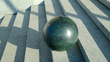 Dark marble sphere on concrete stairs with strong angular shadows