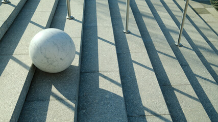 Marble sphere placed on concrete stairs with dramatic shadows